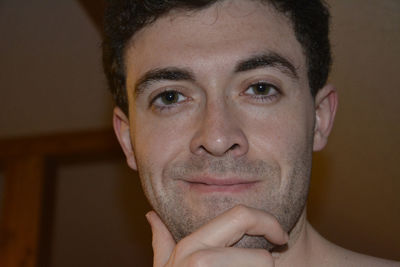 Close-up portrait of smiling young man with hand on chin in darkroom