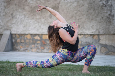 Full length of woman practicing yoga with arms raised on field