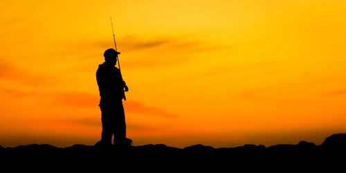 Silhouette man standing against orange sky