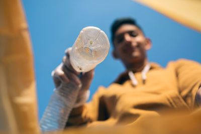 Low angle view of man throwing plastic bottles in bag against sky
