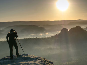 Rear view of man standing on mountain against sky during sunset