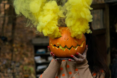 Young beautiful woman holding halloween pumpkin with yellow smoke