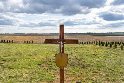 A wooden cross with a statue of jesus with a nameplate without inscriptions standing in an cemetery.