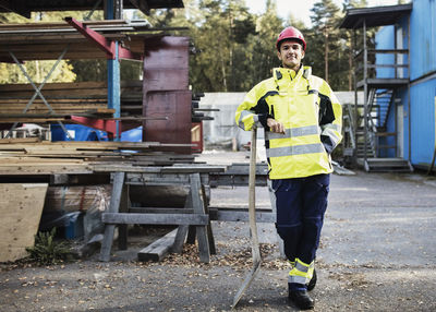 Full length portrait of carpentry student leaning on spade outside school building