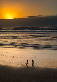 Silhouette people on beach against sky during sunset