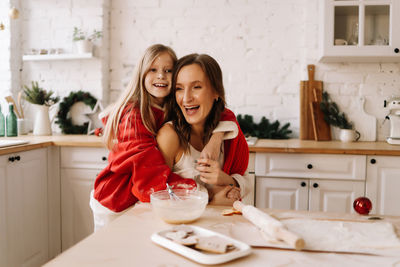 Portrait of smiling and laughing mom and daughter in red sweaters in the kitchen at home