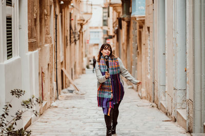 Full length portrait of woman holding monopod standing in alley