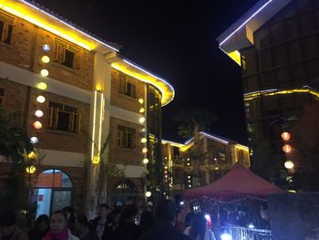 People on illuminated street amidst buildings at night