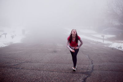 Full length portrait of young woman in snow against sky during foggy weather