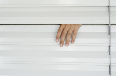 Cropped hand amidst striped blinds