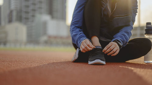 Low section of woman tying shoelace while sitting on sports track