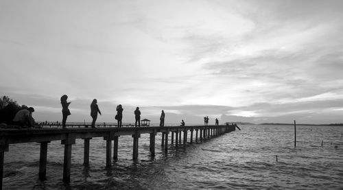 People on pier over sea against sky