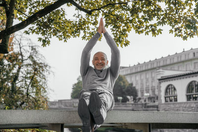 Joyful senior man in grey sweater clapping hands while sitting on a bench