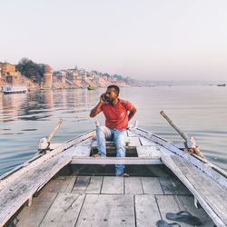 Full length of man sitting on boat in lake against sky