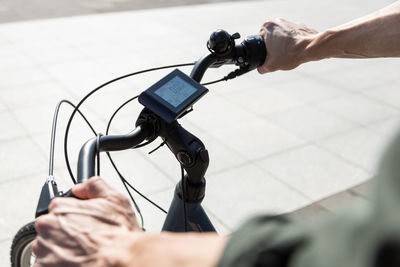 Unrecognizable crop male riding modern electric bicycle with computer display on handlebar in city street