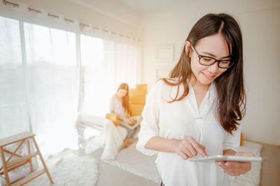 Smiling young woman using digital tablet while standing in home office