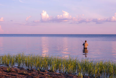 Man standing in sea against sky during sunset