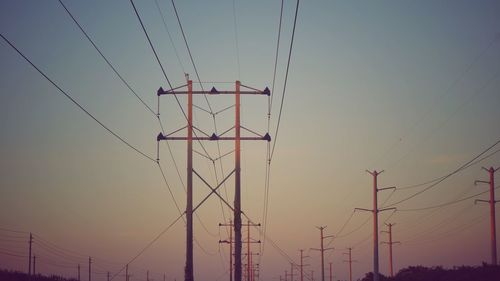 Low angle view of electricity pylon against sky during sunset