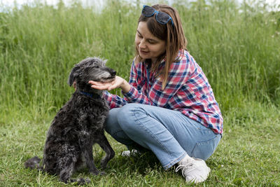 Young woman hugging and petting mixed breed fluffy senior dog bedlington terrier whippet on grass