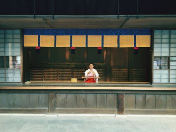 Woman sitting on bench against building