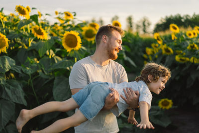 Father with little baby son in sunflowers field during golden hour. 