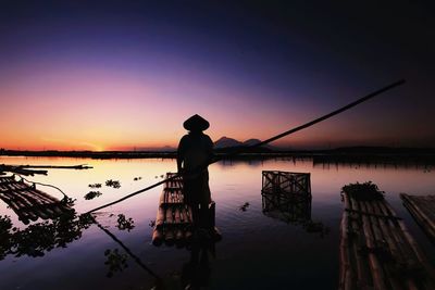 Silhouette man fishing in lake against sky during sunset