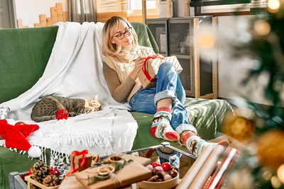Blond woman wrapping presents in recycled card and decorated it with dried oranges and fir branches.