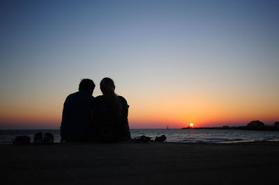 Silhouette couple sitting on promenade against sky during sunset