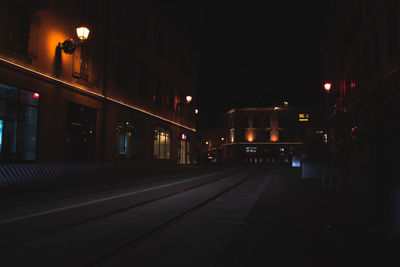 Empty road along illuminated buildings at night