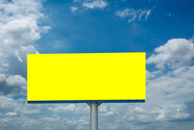 Low angle view of yellow sign against sky