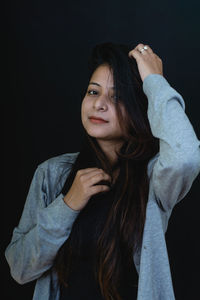 Portrait of young woman standing against black background