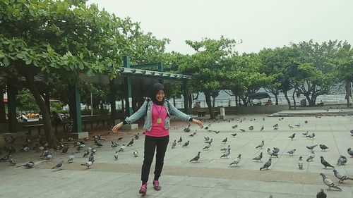 Full length of young woman by birds against sky