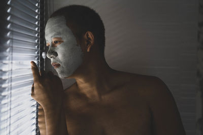 Young man looking through blinds at home