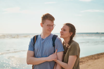 Portrait of young couple standing at beach against sky