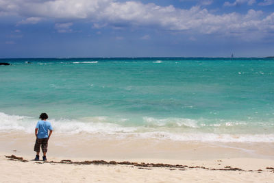 Rear view of man standing at beach against sky