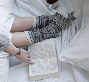 Low section of woman with book on bed