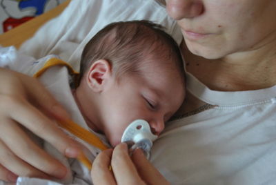 Midsection of mother putting pacifier in son mouth at home