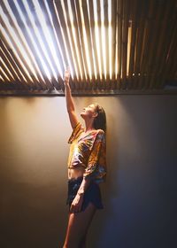 Woman reaching towards ceiling while standing by wall