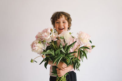 Cheerful happy child with peonys bouquet. smiling little boy on white background.