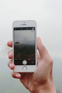 Cropped hand of person photographing nature through mobile phone