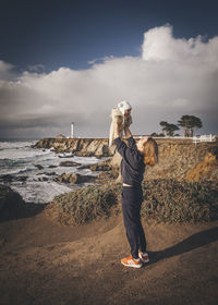 A woman is holding a baby near a lighthouse on the pacific coast