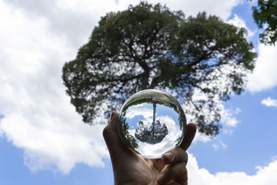 Low angle view of hand holding crystal ball against sky