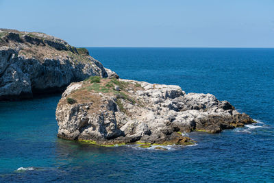 Rock formation in sea against clear blue sky