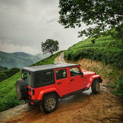 Off-road vehicle parked on mountain against cloudy sky