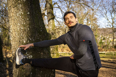 The runner is leaning against an oak tree and is stretching.
