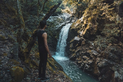 Man standing by waterfall in forest