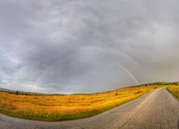 Country road amidst landscape against sky