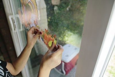 Cropped hands of girl sticking fruits label on window glass at home