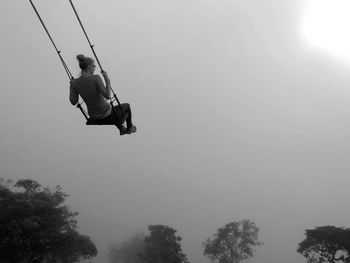 Low angle view of woman on swing against clear sky