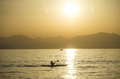 Silhouette man in lake against mountains during sunset